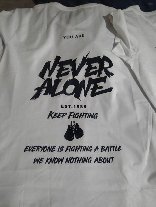 White t-shirt printed You Are Never Alone, Keep Fighting, with boxing gloves and the line everyone is fighting a battle we know nothing about