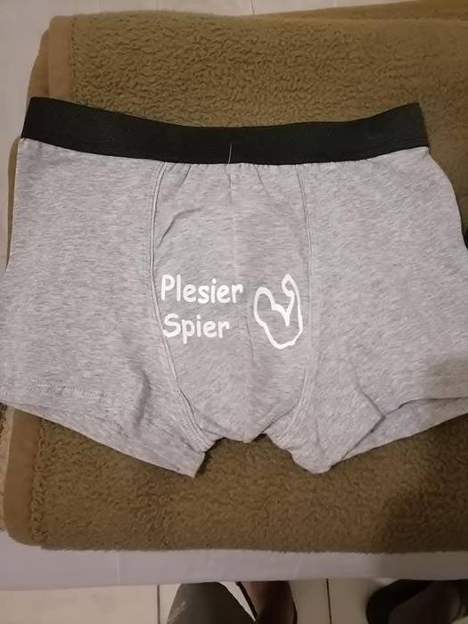 Grey boxer shorts printed Plesier Spier beside a flexed arm